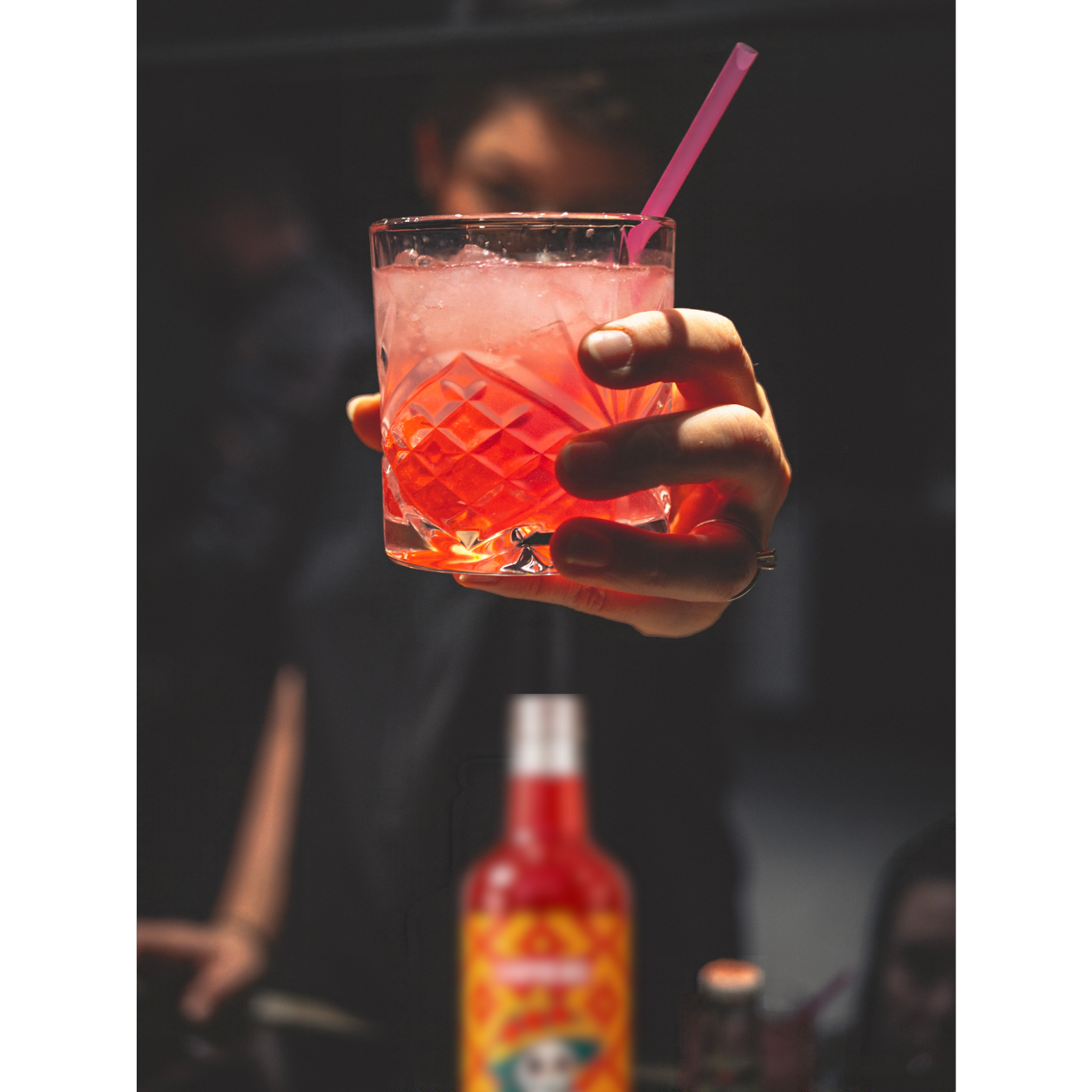 A hand raising a pink iced drink with a Vampiricas bottle in the background